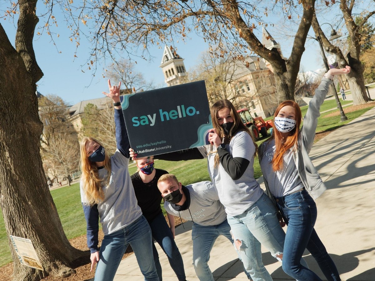 A group of five USU students pose for a photo on the sidewalk in front of Old Main