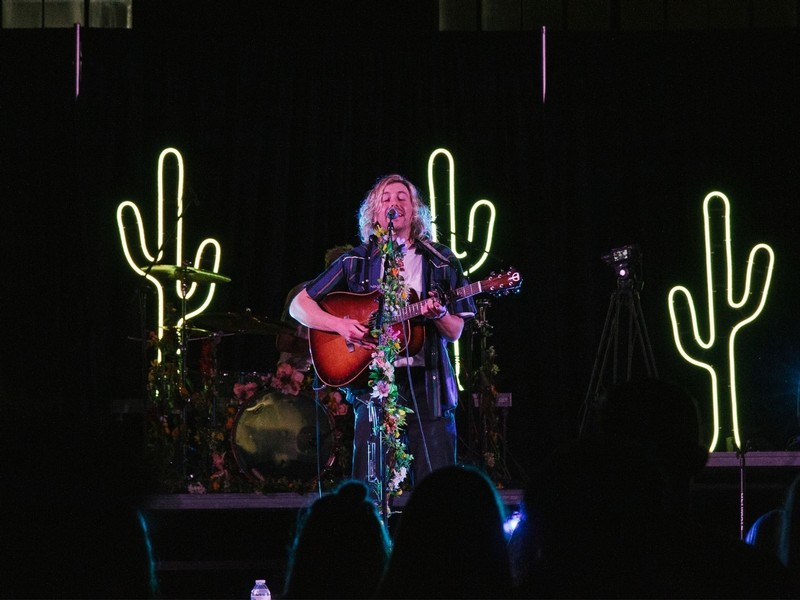 A male singer performs with a guitar on stage in front of a crowd of USU students