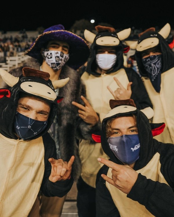 Five male USU students pose for a photo wearing cow costumes in the bleachers at Maverik Stadium