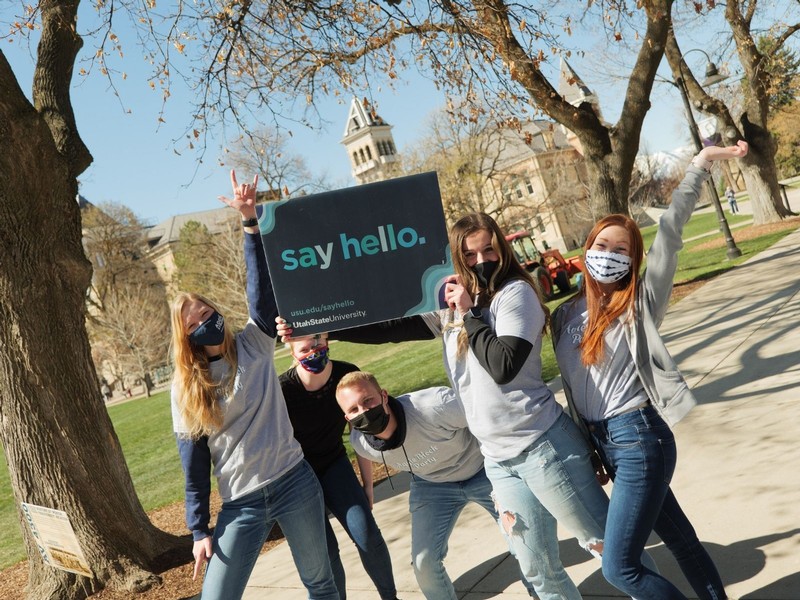 A group of five USU students pose for a photo on the sidewalk in front of Old Main