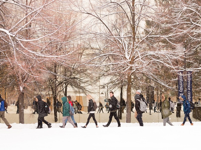 Students walk the wet sidewalk as snow falls during a cold January morning.
