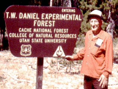 Late USU professor Doc Daniel standing at Forest Service sign