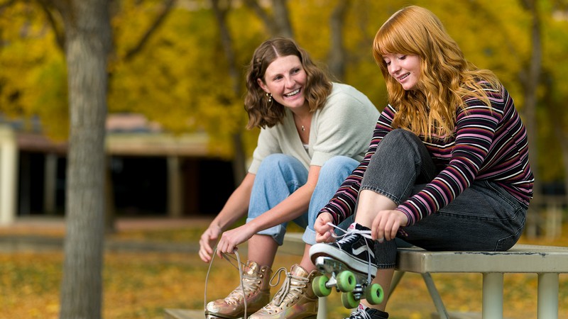 Two women sit on a table while putting on roller skates