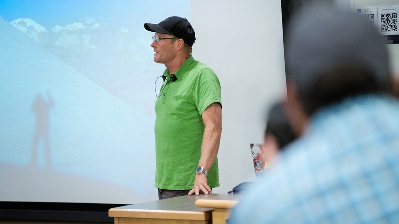 A man speaks in front of a mountaineering slideshow.