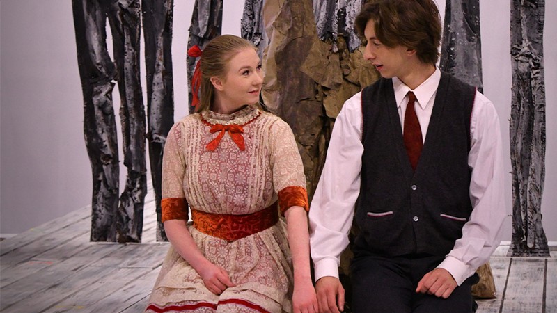Two actors kneeling and holding hands on stage.