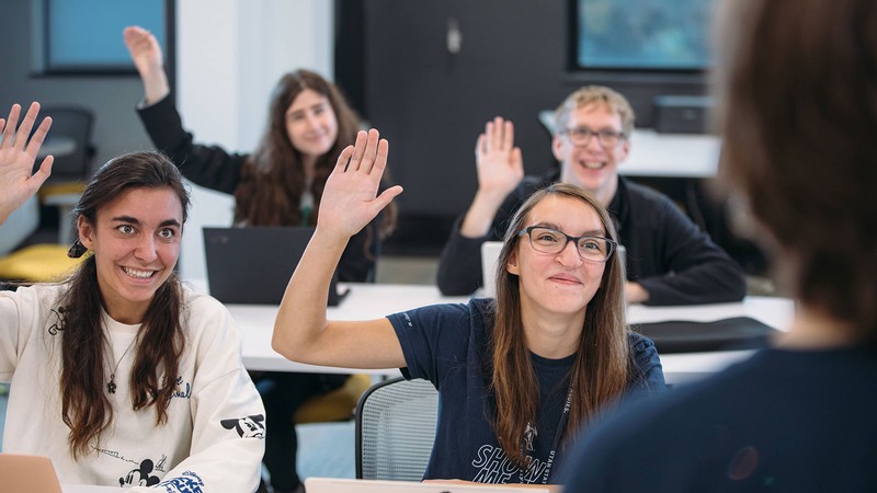 Students raise their hands in a classroom.