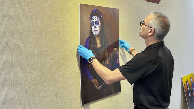 J.P. Spicer-Escalante hanging a photograph of a woman with Day of the Dead skull facepaint.