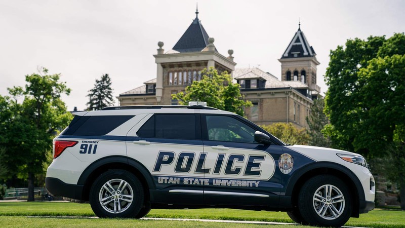 A USU Police Department cruiser parks on the Logan campus Quad with Old Main in the background.