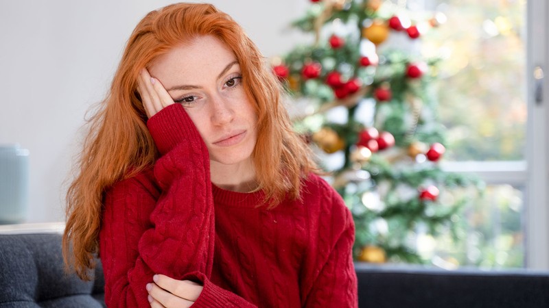 A person with a sad expression in front of a Christmas tree.