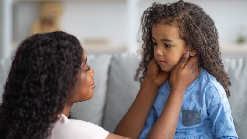 A woman holds a worried child's face in her hands to comfort her.
