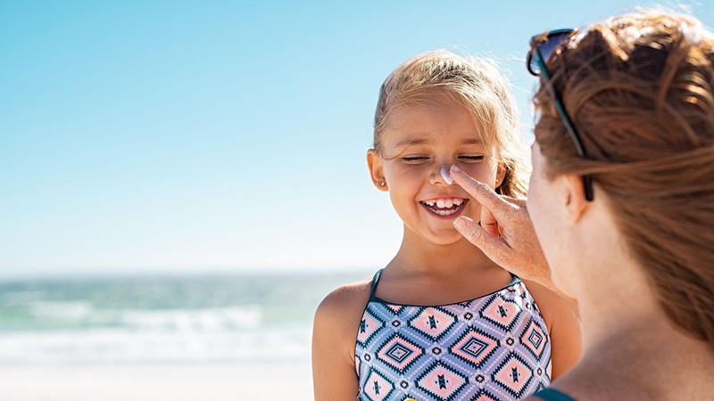 A woman puts sunscreen on a young girl's nose.