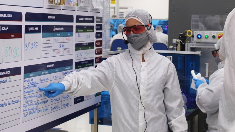 A person wearing protective equipment points to a whiteboard.