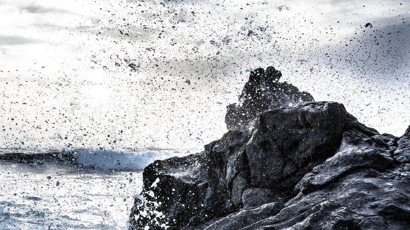 Spray and foam fly through the air after an ocean wave crashes against a rock.