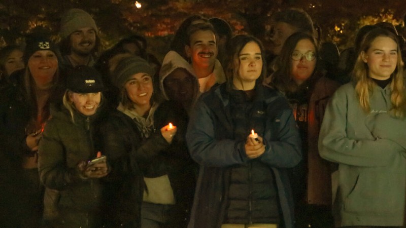 Students holding candles at an outdoor vigil.