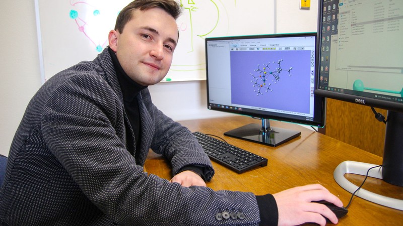 Maksim Kulichenko sits at a computer showing a molecular model.