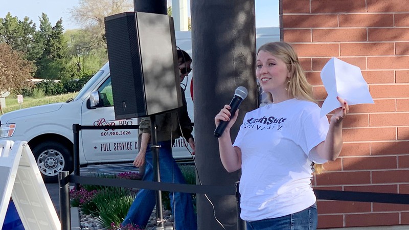 Bailey Lundquist holds a microphone as she speaks outdoors.