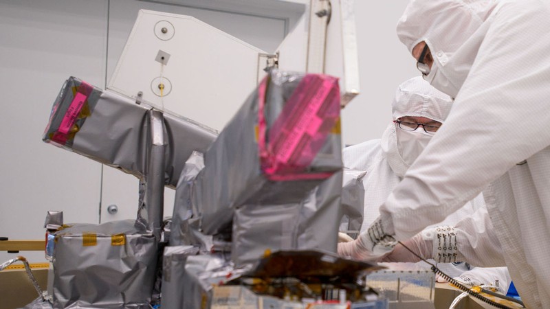 Engineers in protective equipment work on electronics in a cleanroom.