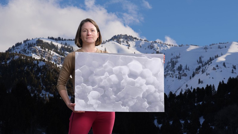 Alexis Ault, standing in front of a mountain range, holds a poster showing a rocky texture.