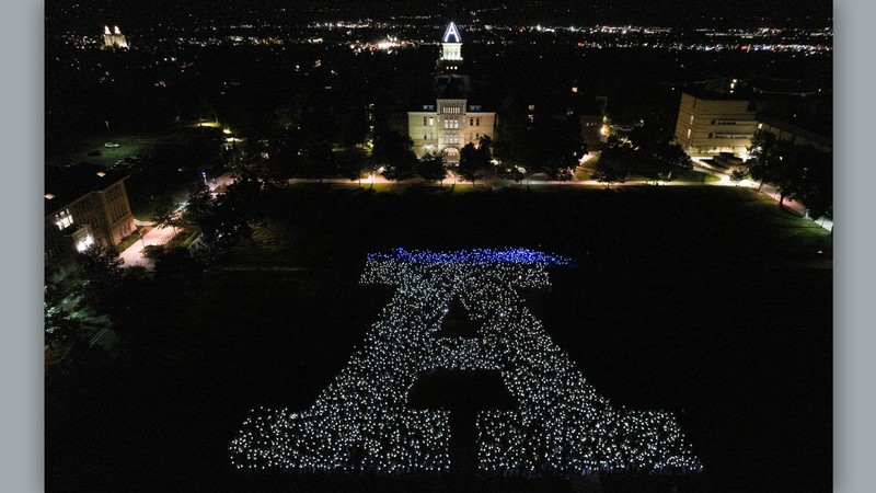 An aerial view of students holding lanterns in the shape of the letter A.