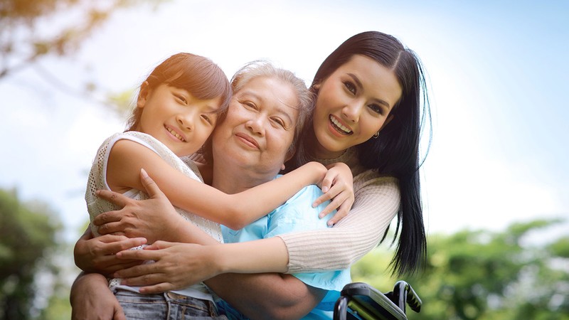 Two people hug a person sitting in a wheelchair.
