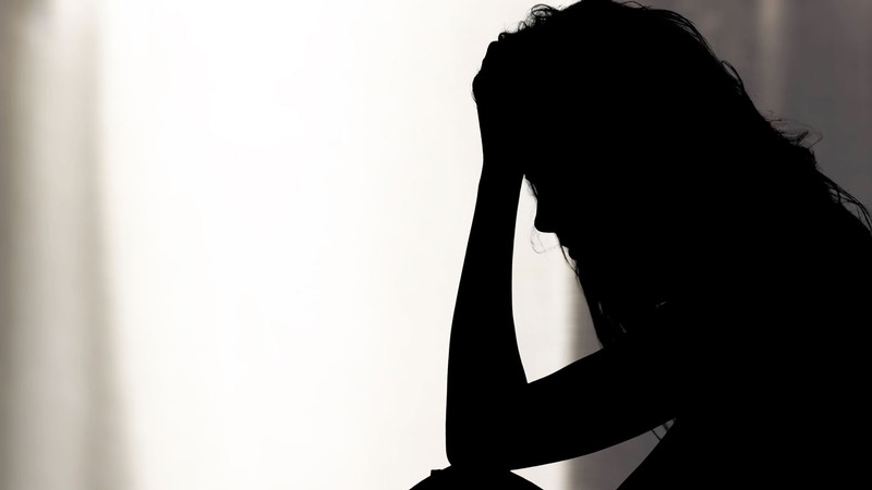 A silhouetted woman rests her forehead on her hand in distress.