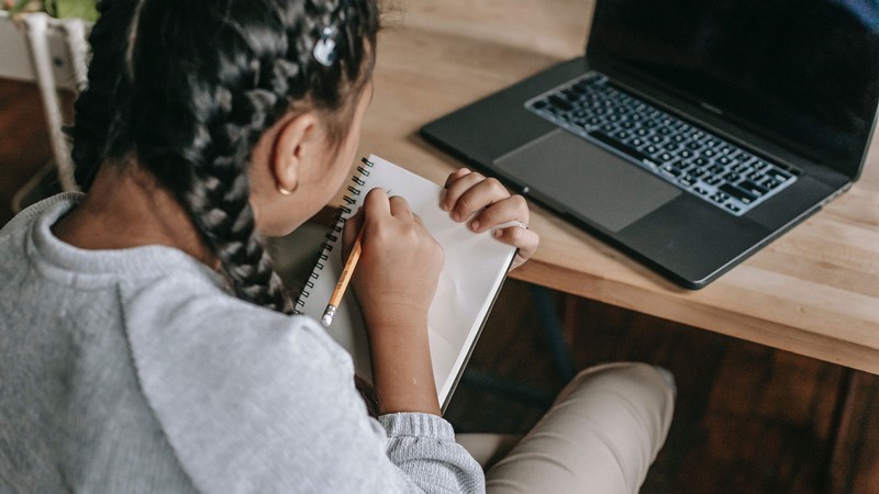 A student in front of a laptop writing in a notebook.