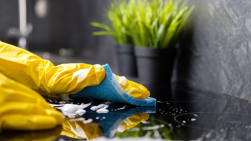 Gloved hands cleaning with a soapy sponge.