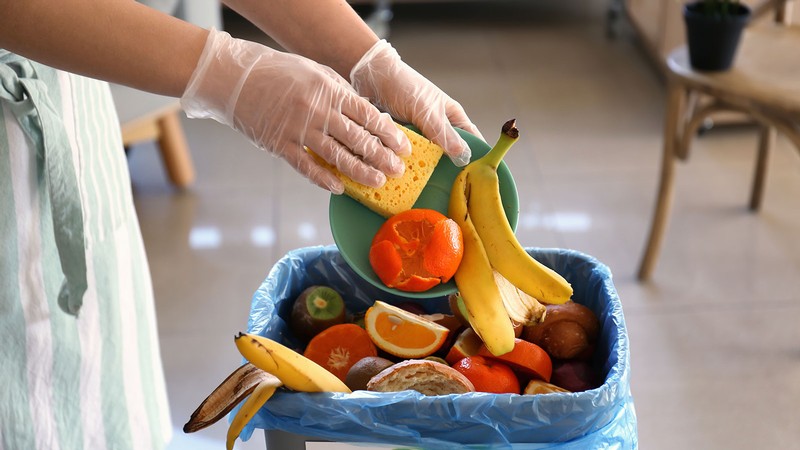 A person scraping fruit peels into a compost bin.