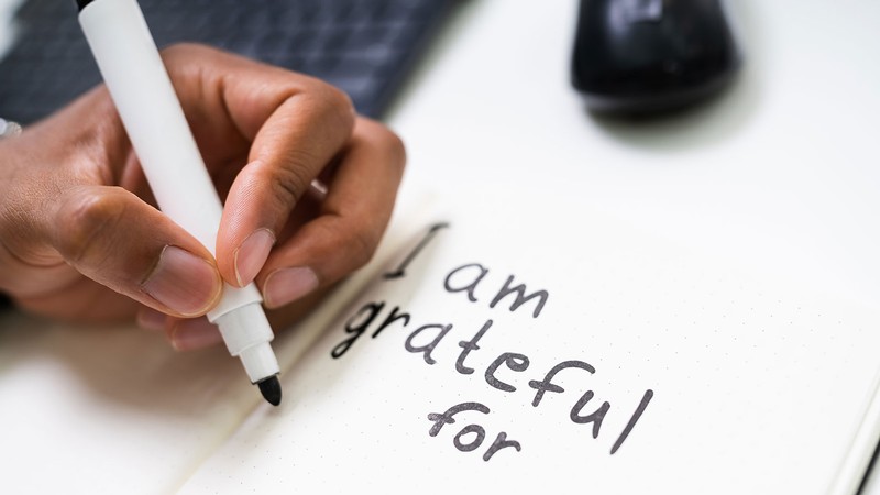 A person writing in a journal. Text reads: I am grateful for.