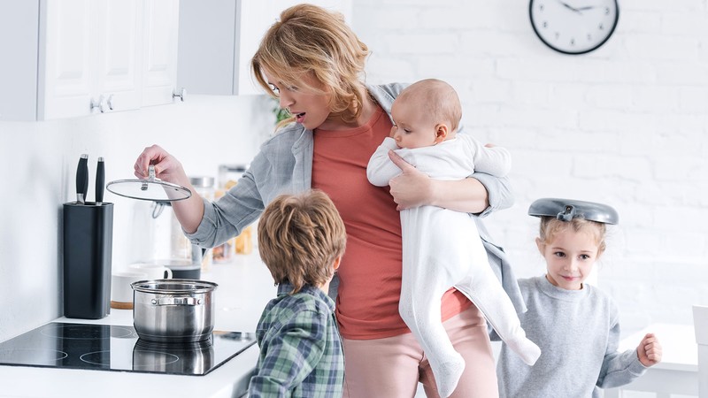 A mother checking a pot while tending three children.