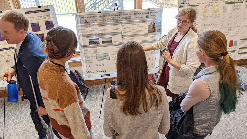 A grad student explaining a research poster to others.
