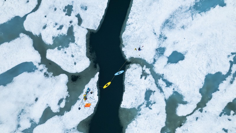 An aerial view of kayaks on a river through an ice floe.