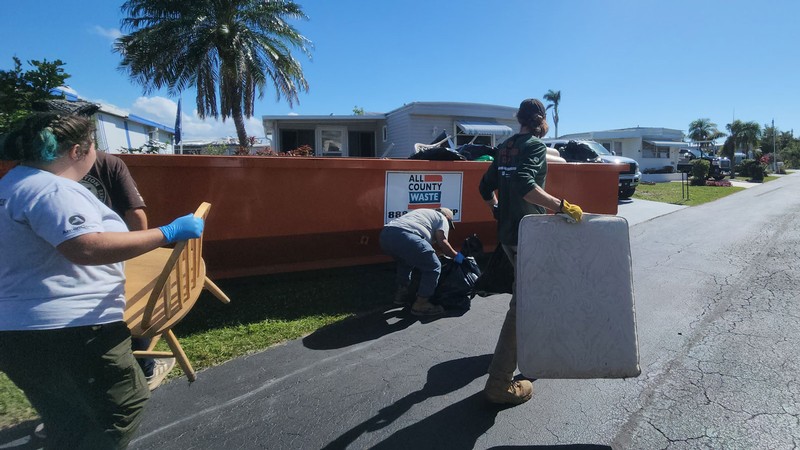 Utah Conservation Corps members carry items toward a dumpster.