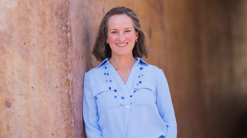 A woman poses for a photo against a stone wall.