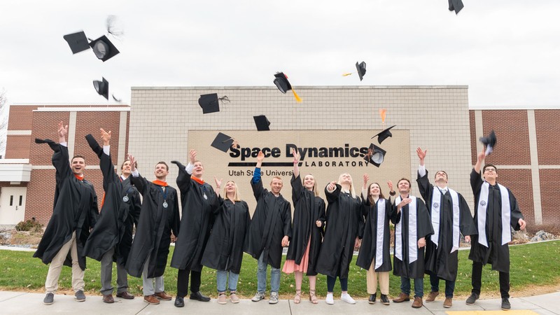 Students throwing mortarboards in the air outside an SDL building.