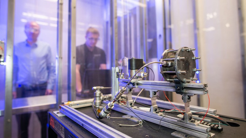 Engineers behind glass test a satellite propulsion device.