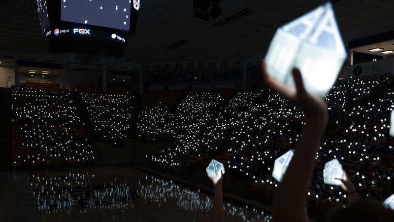 People in a stadium holding A-shaped lanterns.