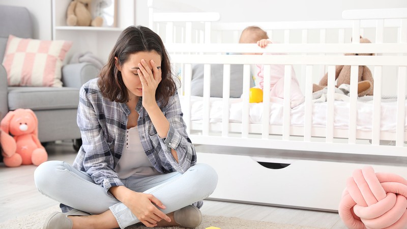 A woman holding her face in front of a crib.