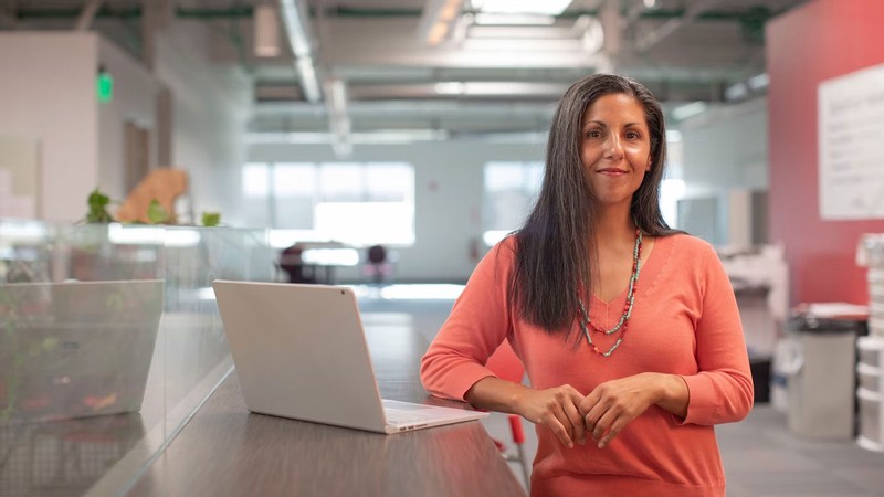 A woman standing at a laptop in an office.