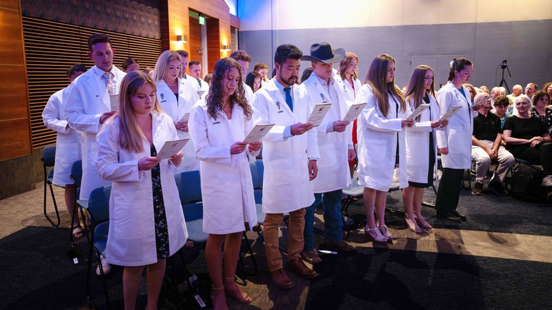 Students in white coats reading an oath.