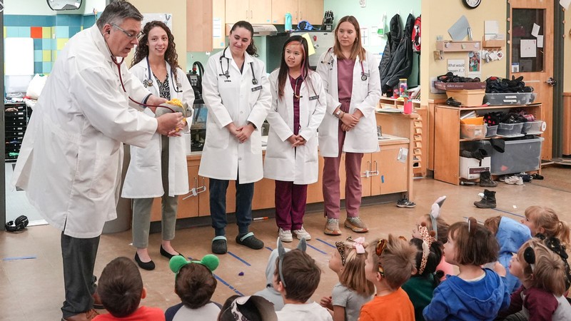A veterinarian and students demonstrating a stethoscope to preschoolers in a classroom.
