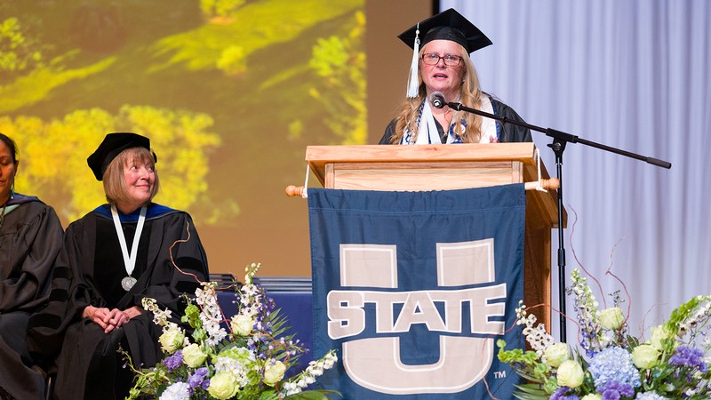 A student in graduation regalia gives a speech.