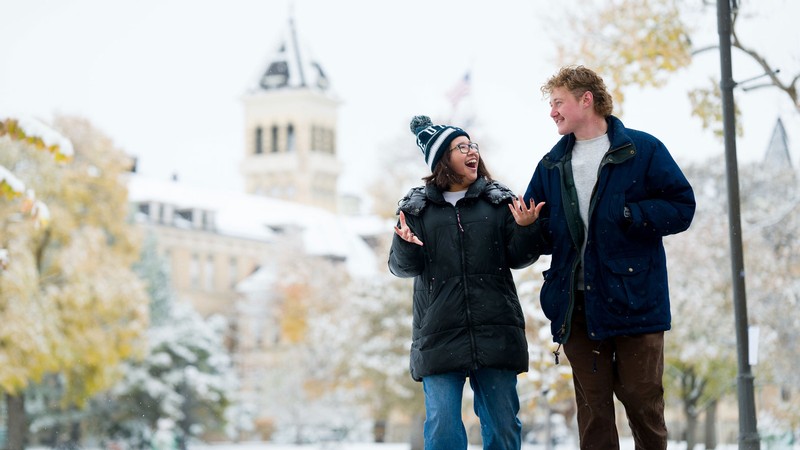 Two people walking in the snow in front of Old Main.