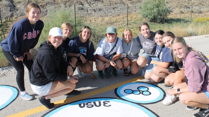 People gather around a street painting that says "USU E."