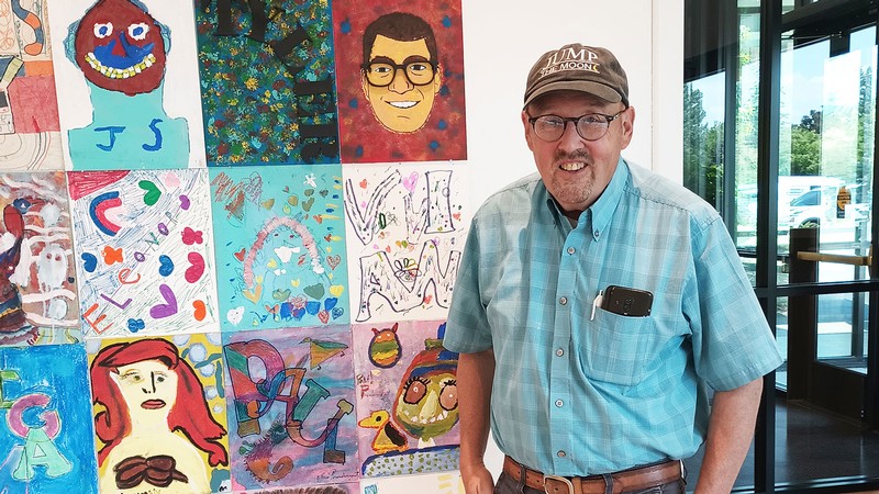 Michael Bingham stands next to an art collage.