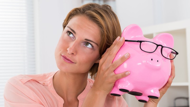 A woman putting her ear to a piggy bank.