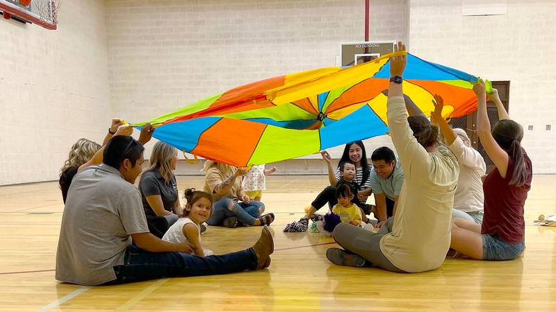Parents and children play with a parachute in a school gym.