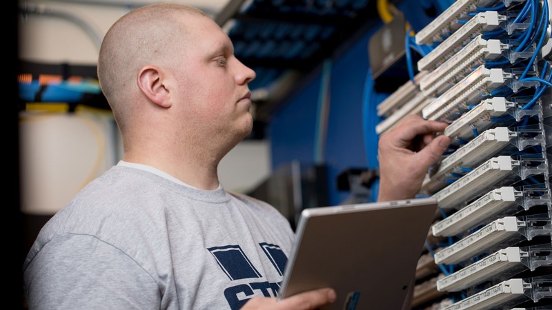 A worker inspecting computer networking hardware.