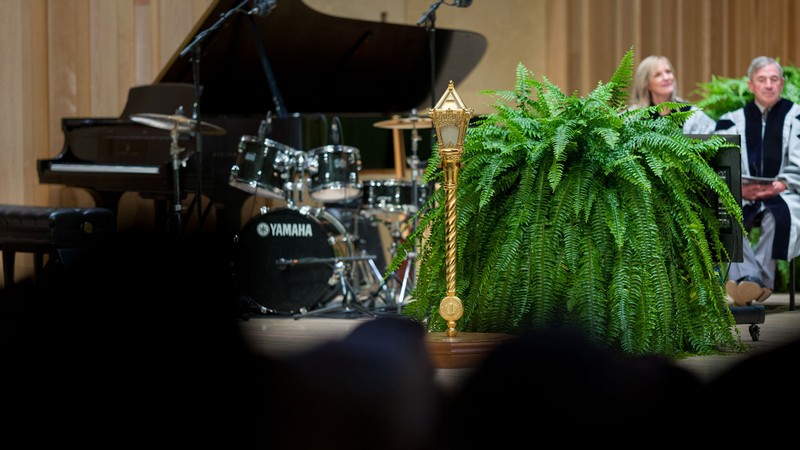 A golden mace topped with the letter A sits on a stage.