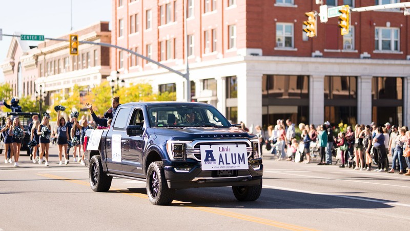 A truck with an oversize USU license plate reading "Alum" in a parade.